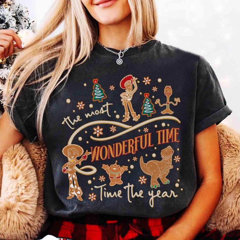 Puede incluir: Camiseta gris oscuro con personajes de Toy Story estilo pan de jengibre, incluyendo a Woody y Jessie, con el texto "The most wonderful time of the year". El dise&ntilde;o incluye copos de nieve y &aacute;rboles de Navidad.