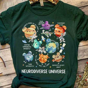Op de afbeelding: Groen T-shirt met een afbeelding van planeten en sterren. De tekst "Celebrate Minds of All Kinds" en "Neurodiverse Universe" staat op het T-shirt gedrukt.