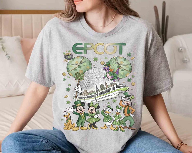 May include: A grey t-shirt with a St. Patrick's Day theme, displaying the word "EPCOT" in green and gold. The design includes Mickey Mouse, Minnie Mouse, Donald Duck, Daisy Duck, Goofy, and Pluto in green attire, alongside a monorail and Spaceship Earth.