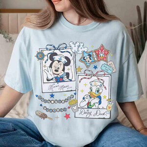 May include: Light blue t-shirt featuring Minnie Mouse and Donald Duck in sailor outfits. The shirt includes framed illustrations, stars, and the text "Minnie Mouse xoxo" and "Daisy, Duck".