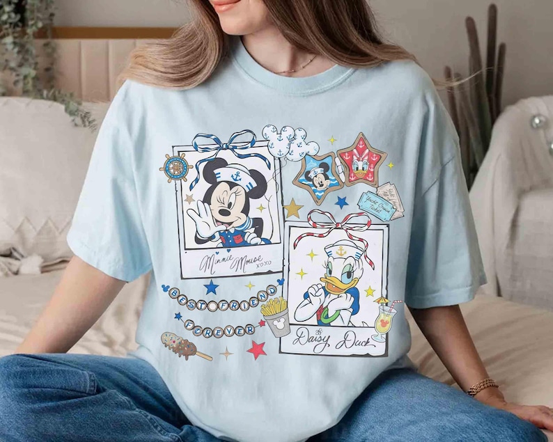 May include: Light blue t-shirt featuring Minnie Mouse and Donald Duck in sailor outfits. The shirt includes framed illustrations, stars, and the text "Minnie Mouse xoxo" and "Daisy, Duck".