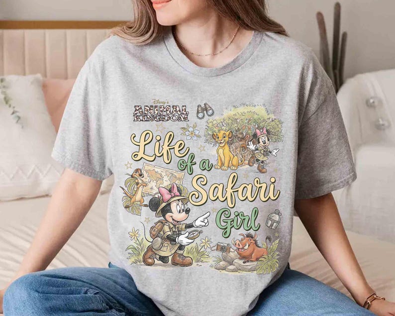 May include: A gray t-shirt featuring a colorful graphic design with the text "Life of a Safari Girl." The design includes cartoon characters, a map, and the words "Disney's Animal Kingdom."