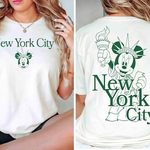 May include: Off-white t-shirt with a green graphic of Minnie Mouse as the Statue of Liberty, holding a torch. The text "New York City" is above and below the graphic. The front of the shirt has the text "New York City" and a Minnie Mouse graphic.