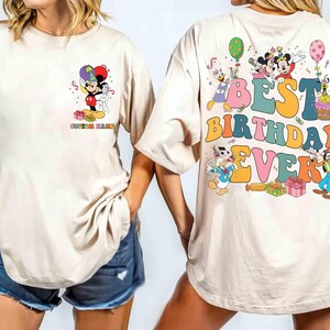 Pu&ograve; includere: T-shirt beige con grafica colorata di Topolino e amici, palloncini e regali. La parte posteriore della maglietta dice "BEST BIRTHDAY EVER". La maglietta ha una vestibilit&agrave; ampia.