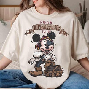 Puede incluir: Una camiseta blanca con una imagen de dibujos animados de Mickey Mouse vestido de pirata. El texto "Yo Ho, Yo Ho, A Pirates Life For Me!" est&aacute; impreso sobre Mickey Mouse.