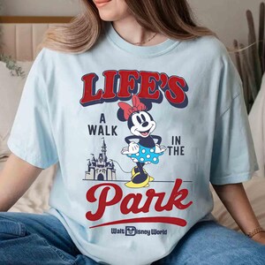 May include: Light blue t-shirt featuring Minnie Mouse with the text "LIFE'S A WALK IN THE PARK" in red and blue. Minnie Mouse is wearing a polka dot skirt and a red bow. The Walt Disney World logo is at the bottom.