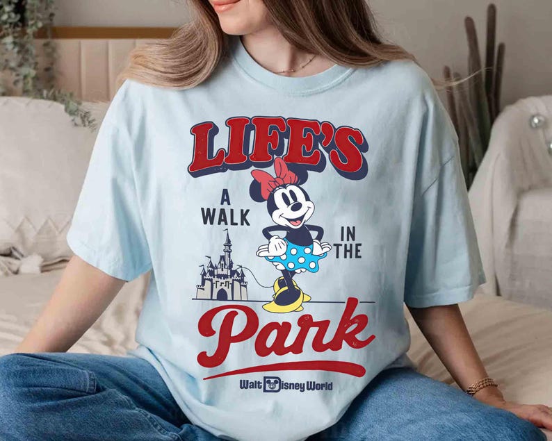 May include: Light blue t-shirt featuring Minnie Mouse with the text "LIFE'S A WALK IN THE PARK" in red and blue. Minnie Mouse is wearing a polka dot skirt and a red bow. The Walt Disney World logo is at the bottom.