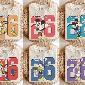 May include: Cream-colored t-shirts featuring various Disney characters and the text "Class of '26". Designs include Pluto, Mickey Mouse, Minnie Mouse, Goofy, Donald Duck, and Daisy Duck, each set against a colorful number 26.