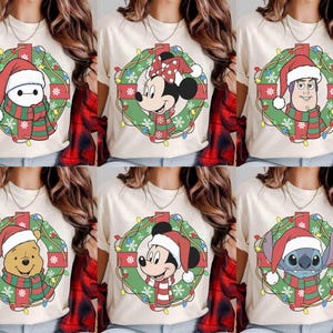 Op de afbeelding: Cr&egrave;mekleurige T-shirts met kerstthema Disney-personageontwerpen. Elk shirt toont een personage zoals Baymax, Minnie Mouse, Buzz Lightyear, Winnie de Poeh, Mickey Mouse en Stitch, allemaal met kerstmutsen en sjaals in een krans.