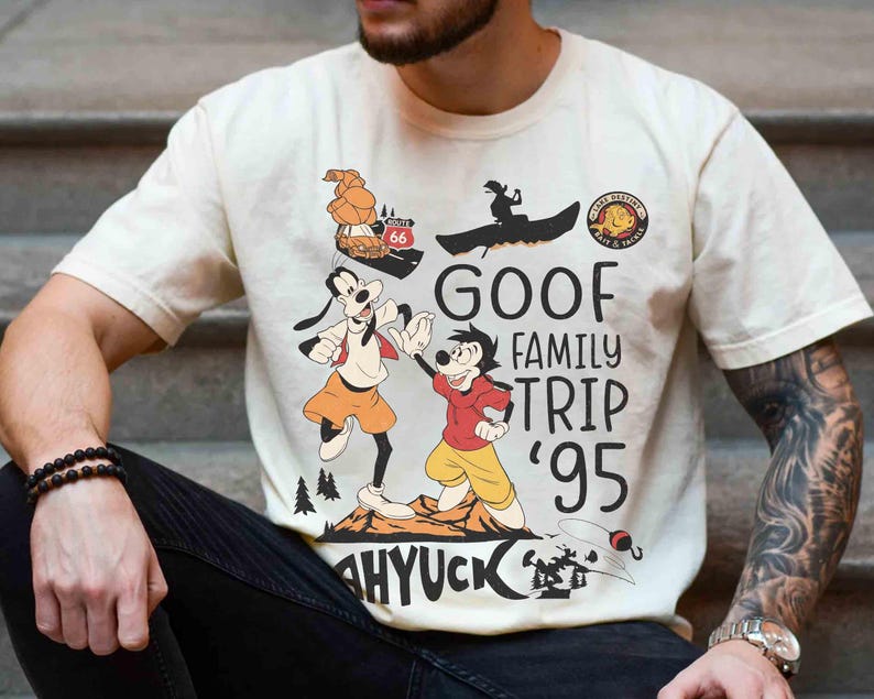 Pode incluir: Camiseta creme com um gr&aacute;fico de Pateta e Max da s&eacute;rie de televis&atilde;o Goof Troop da Disney. O design inclui o texto "GOOF FAMILY TRIP '95" e ilustra&ccedil;&otilde;es de viagem. A camiseta tem mangas curtas.