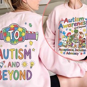 May include: A light pink sweatshirt with the words "Autism Awareness and Beyond" in colorful text. The design includes cartoon characters and puzzle pieces. The back of the sweatshirt has the words "Autism and Beyond" with a puzzle piece design.