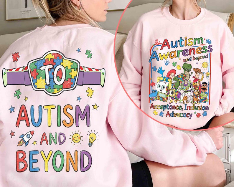 May include: A light pink sweatshirt with the words "Autism Awareness and Beyond" in colorful text. The design includes cartoon characters and puzzle pieces. The back of the sweatshirt has the words "Autism and Beyond" with a puzzle piece design.