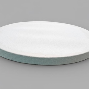 Puede incluir: Una fuente redonda de cerámica blanca con una superficie ligeramente texturizada. La fuente tiene un borde azul claro y se encuentra sobre un fondo gris. Adecuada para servir aperitivos o postres.