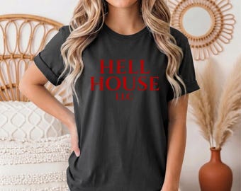 May include: A heather black short-sleeve t-shirt featuring the red text HELL HOUSE LLC printed on the front. The shirt is a Bella Canvas 3001 model, characterized by a crew neckline and a standard fit, shown in a casual, everyday style.