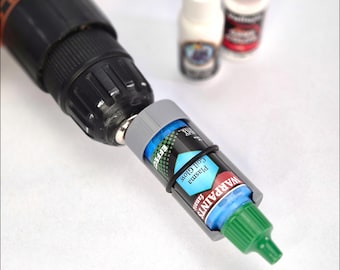 May include: A drill paint shaker with a bottle of blue paint secured inside. The paint bottle is labeled "Plasma Coil Glow" and is held in place with a black rubber band. Other paint bottles are in the background.