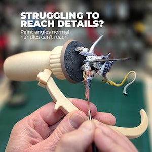 Op de afbeelding: Een beige schilderhandvat met een miniatuurbeeldje. De tekst luidt: "STRUGGLING TO REACH DETAILS?" en "Paint angles normal handles can't reach". Het beeldje is beschilderd met meerdere kleuren.