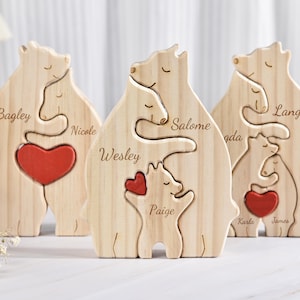 Pode incluir: Três peças de quebra-cabeça de madeira em forma de família de ursos com corações vermelhos. Os ursos se abraçam e têm nomes gravados: Bagley, Nicole, Wesley, Salome, Paige, Lange, Karla e James.