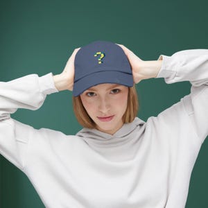 May include: A navy blue baseball cap with a distressed look and a yellow question mark embroidered on the front.