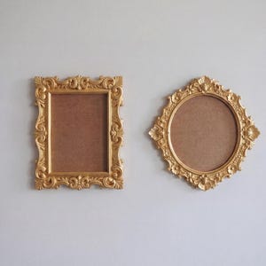 Pode incluir: Duas molduras douradas ornamentadas. Uma é retangular, a outra é redonda com uma borda externa em forma de diamante. Ambas as molduras têm intrincados arabescos e um acabamento dourado, com um fundo marrom.