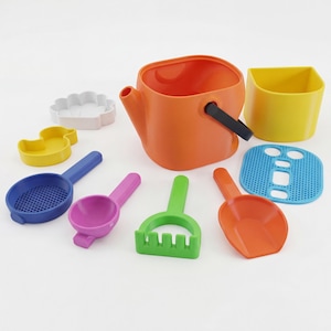 May include: A collection of colorful plastic beach toys, including a bright orange watering can, a yellow bucket, and various scoops, rakes, and molds in blue, green, pink, and orange. The set is designed for children's play.