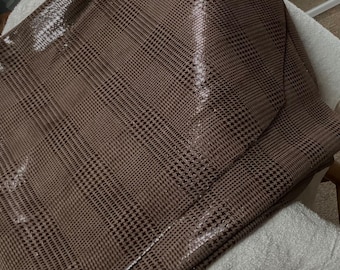 May include: A brown fabric with a houndstooth pattern. The fabric has a slight sheen and is folded in half.