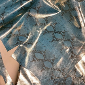 May include: A piece of teal blue snakeskin fabric with a metallic sheen. The fabric is folded and has a textured surface.