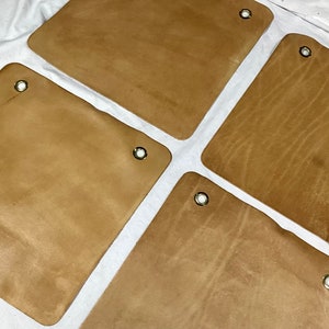 K&ouml;nnte beinhalten: Vier braune Lederquadrate mit Messing&ouml;sen. Das Leder hat eine nat&uuml;rliche Maserung.