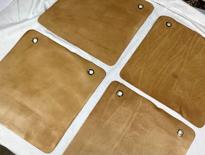 K&ouml;nnte beinhalten: Vier braune Lederquadrate mit Messing&ouml;sen. Das Leder hat eine nat&uuml;rliche Maserung.