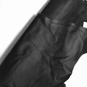 May include: Black fabric with a textured surface. The fabric is folded and appears to be a type of mesh or netting.