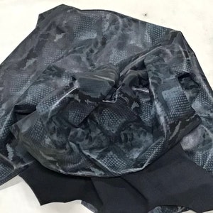 May include: A close-up of a black and gray snakeskin patterned fabric. The fabric is folded and crumpled, showing the texture and pattern.