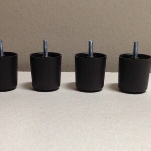 May include: Four brown plastic furniture legs with a threaded metal screw in the center of each leg.