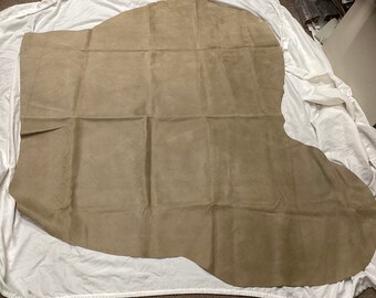 May include: A large piece of light brown suede leather. The leather is folded in half and has a slightly irregular shape.