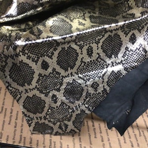 May include: Close-up of a gold and black snakeskin fabric with a black fabric border.