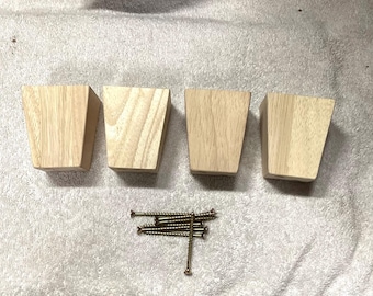 Könnte beinhalten: Vier unbehandelte Möbelbeine aus Holz mit quadratischer Basis und abgeschrägter Oberkante. Die Beine sind in einer Reihe auf einer weißen Oberfläche angeordnet. Ein Stapel goldener Schrauben ist ebenfalls auf dem Bild zu sehen.