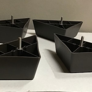 May include: Four black triangular furniture legs with a threaded screw in the center of each leg.