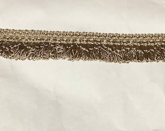 Könnte beinhalten: Nahaufnahme einer beige Fransenborte mit gewebter Textur. Die Fransen sind etwa 2,5 cm lang und aus einem weichen, biegsamen Material gefertigt.
