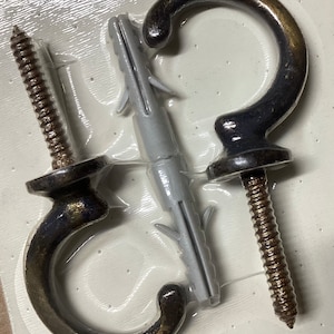 May include: Two black metal hooks with gold accents and screws. The hooks are packaged on a white plastic backing with gray plastic anchors.