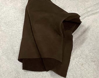 May include: A folded piece of dark brown leather, possibly for crafting or upholstery. The leather has a smooth, matte finish and appears to be a single, uncut piece. The fabric is draped over a light gray surface.