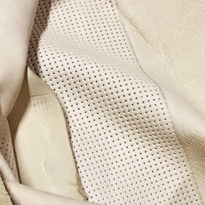 May include: Close-up of a white leather material with a perforated pattern. The leather is folded over, revealing a smooth, unperforated side.