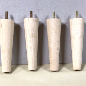 May include: Four wooden furniture legs with a tapered design and a threaded metal top. The legs are light brown in color and are arranged in a row.
