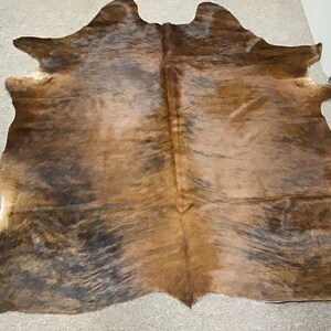 K&ouml;nnte beinhalten: Ein brauner und schwarzer Kuhfellteppich mit einem nat&uuml;rlichen, abgenutzten Look. Der Teppich hat ein langes, flie&szlig;endes Haar und ein einzigartiges Muster.