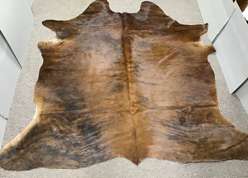 K&ouml;nnte beinhalten: Ein brauner und schwarzer Kuhfellteppich mit einem nat&uuml;rlichen, abgenutzten Look. Der Teppich hat ein langes, flie&szlig;endes Haar und ein einzigartiges Muster.