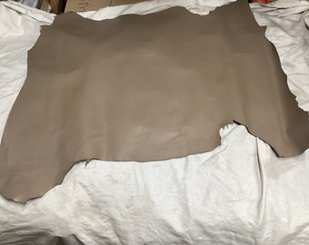May include: A large piece of light brown leather with an irregular shape. The leather is smooth and appears to be supple.