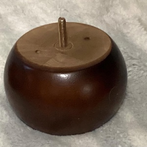 May include: A dark brown, round wooden furniture leg with a flat, light brown top. A threaded metal rod extends from the top for attachment. The leg has a smooth, glossy finish and is designed for furniture.