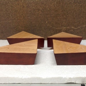 May include: Four triangular wooden furniture legs with a reddish-brown stain. The legs are arranged in a row on a white surface.