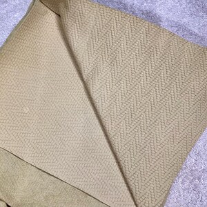 May include: A beige fabric with a textured pattern of small, repeating diamonds. The fabric is folded in half, revealing the pattern on both sides.