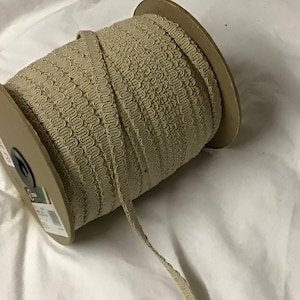 May include: A spool of beige trim with a decorative, looped pattern. The trim is wound around a cardboard spool.
