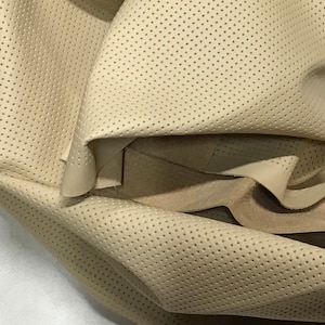 May include: Close-up of a beige fabric with a perforated pattern. The fabric is folded and shows the texture of the material.