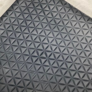 May include: Close-up of a dark gray, textured surface with a repeating triangular pattern. The pattern creates a three-dimensional effect, with each triangle slightly raised. The surface appears to be made of a flexible material.