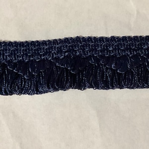 May include: Navy blue fringe trim with a woven texture. The fringe is approximately 1 inch long.